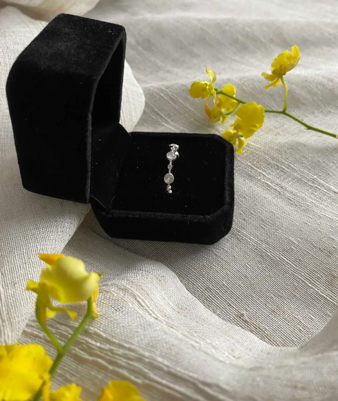 Lấy cảm hứng từ vẻ lấp lánh trong trẻo của những viên đá nhỏ như những giọt ánh trăng rơi xuống nền nhung đen huyền bí.
Thân nhẫn làm bằng kim loại sáng bạc, được điểm xuyết bởi ba viên đá nhỏ tròn, sắp xếp theo chiều dọc.
Mỗi viên đá tỏa sáng nhẹ nhàng, phản chiếu ánh sáng tự nhiên một cách thanh lịch
Tổng thể mang lại cảm giác tinh khiết, tối giản nhưng vẫn đầy quyến rũ — phù hợp với người yêu thích phong cách thanh lịch và nhẹ nhàng.